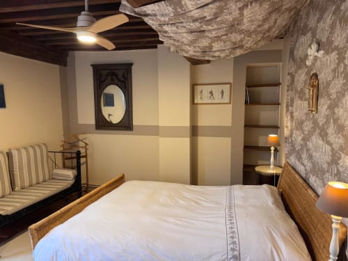 Chambre du gîte La Maison du Petit Louis avec lit, fauteuil rayé, plafond à motifs, éléments en bois et vue sur le jardin