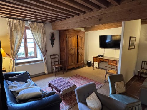 Spacieux séjour aux poutres apparentes, cheminée, télévision, mobilier d'époque et vue sur le jardin au Gîte La Maison du Petit