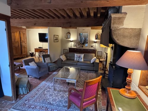 Élégant séjour du Gîte La Maison du Petit Louis avec poutres apparentes, canapé gris, fauteuil mauve et cheminée