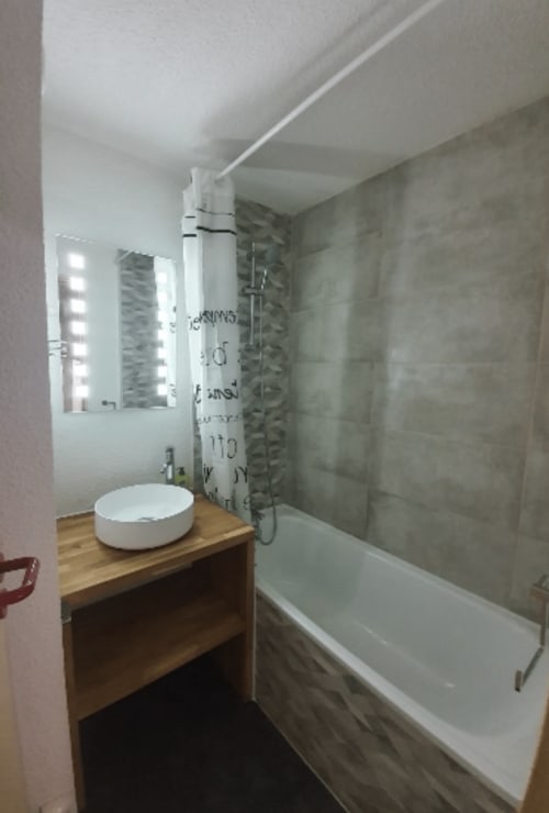 Salle de bains moderne de l'appartement Vars avec lavabo rond blanc, meuble-vasque en bois, miroir éclairant et baignoire avec douche