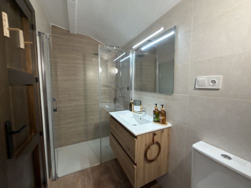 Baño moderno en habitación Alquería de Casa La Almedina, Casarabonela con ducha, tocador de madera e iluminación de espejo
