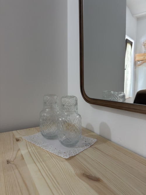 Cristalería con patrones geométricos sobre tapete de encaje blanco junto a espejo en la habitación de Casa La Almedina