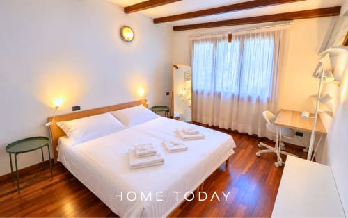 Camera da letto luminosa nell'appartamento Hometoday a Padova, con biancheria bianca, travi in legno e ampie finestre