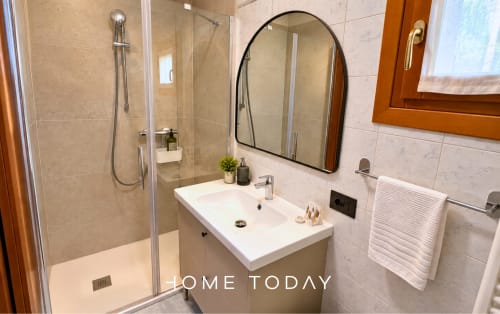 Bagno moderno nell'appartamento Hometoday a Padova con doccia in vetro, lavabo bianco, specchio ad arco e scaldasalviette elettrico