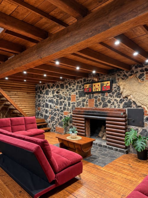 Rustic Master Suite at Cabañas el Encanto with exposed beams, stone fireplace, red seating, and wooden floors in Las Vigas,
