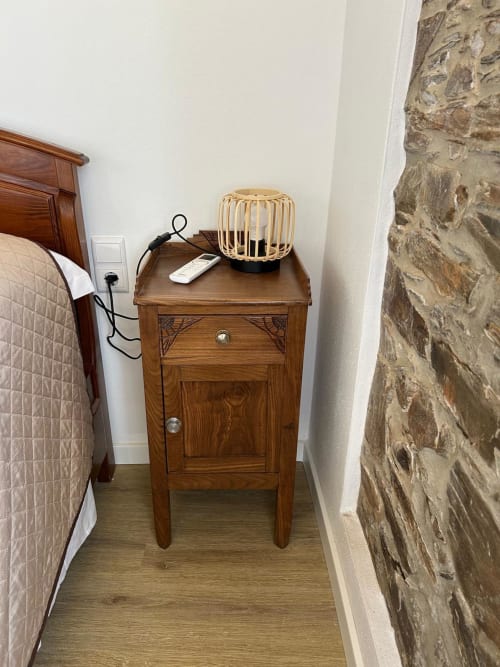 Criado de cabeceira em madeira com luminária de palha no quarto da casa Curral em Casas do Sinhel, parede de pedra visível