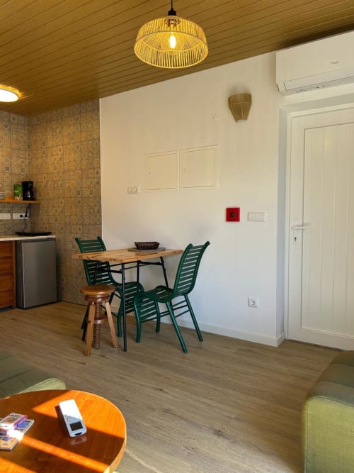 Espaço de estar em cottage nas Casas do Sinhel com área de refeições, cadeiras verdes, kitchenette e detalhes em madeira em Alvares.
