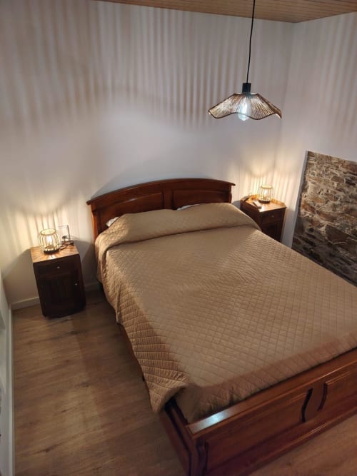 Quarto aconchegante na casa rural Casas do Sinhel em Álvares com cama de madeira, luminária pendente e detalhes em pedra