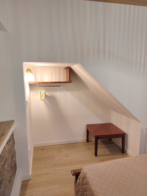 Aconchegante área de estar de chalé com banco de madeira, mesa escura, vigas aparentes e cabideiro sob teto inclinado com luz natural