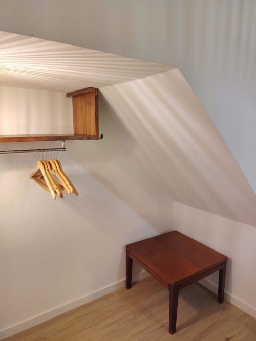 Armário do quarto sob o telhado com prateleira de madeira, varão metálico com cabideiros e banco na Casa do Sinhel em Álvares