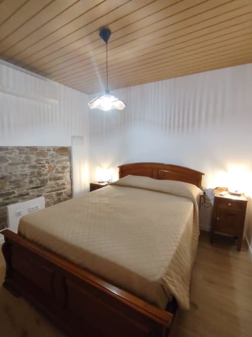 Quarto aconchegante na casa rural Casas do Sinhel em Alvares, com cama de madeira, parede de pedra e luminária pendente