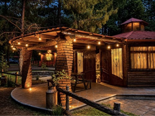 Suite Cabaña Roble en Cabañas el Encanto iluminada al atardecer con chimenea de ladrillo, puertas de madera y luces decorativas en Las