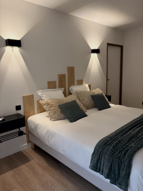 Chambre moderne à l'Hôtel les Vieilles Pierres à Eymet avec lit en bois, draps blancs, éclairages d'ambiance et mobilier foncé