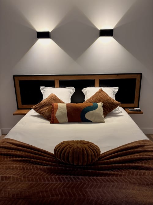 Chambre moderne à l'Hôtel les Vieilles Pierres avec tête de lit en bois, literie blanche, coussins décoratifs et applique murale