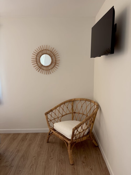 Coin de chambre moderne à l'Hôtel les Vieilles Pierres avec fauteuil en rotin tressé, miroir soleil décoratif et applique murale