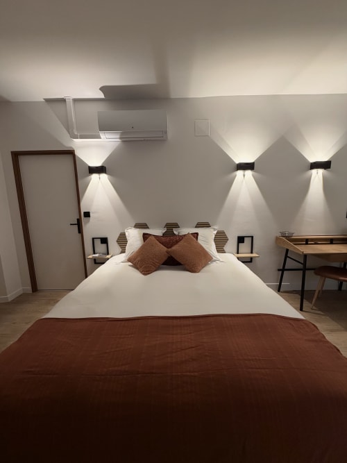 Chambre moderne à l'Hôtel les Vieilles Pierres à Eymet avec lit queen-size, accents marron, appliques murales et climatisation