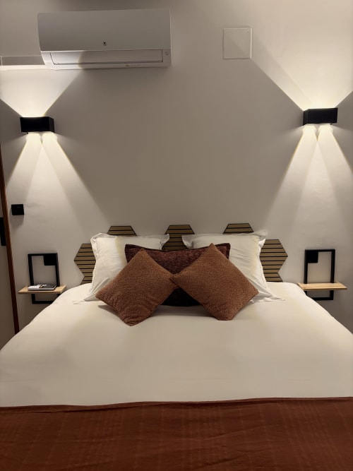 Chambre moderne de l'Hôtel les Vieilles Pierres avec lit blanc, coussins marron et appliques murales contemporaines à Eymet
