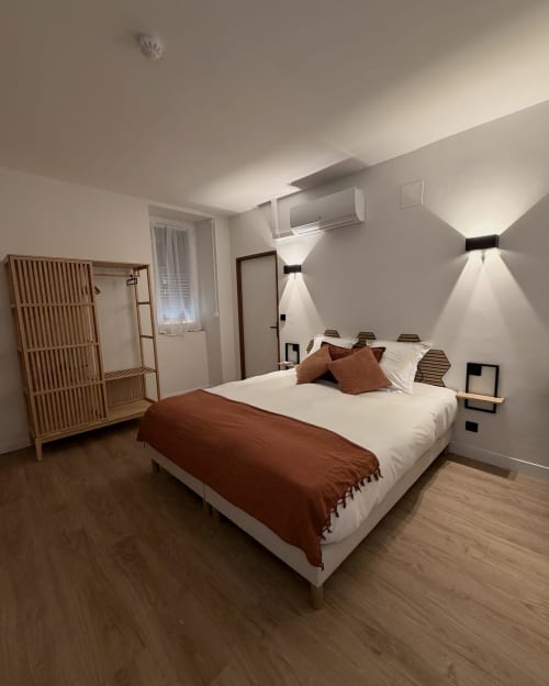 Chambre moderne à l'Hôtel les Vieilles Pierres à Eymet avec lit queen-size, armoire en bois et éclairage mural ambiant