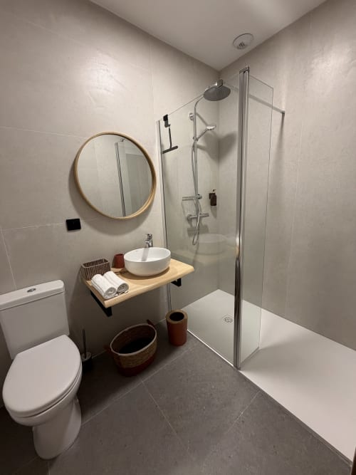 Salle de bains moderne de l'Hôtel les Vieilles Pierres avec douche à l'italienne, miroir rond et meuble-lavabo en bois à Eymet