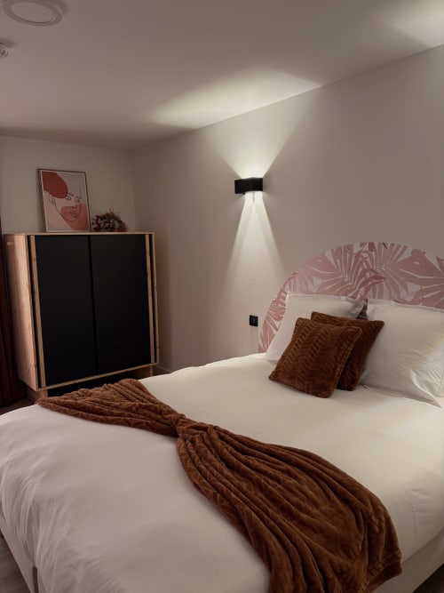 Chambre moderne à l'Hôtel les Vieilles Pierres à Eymet avec lit blanc, tête de lit rose, coussins marron et design contemporain