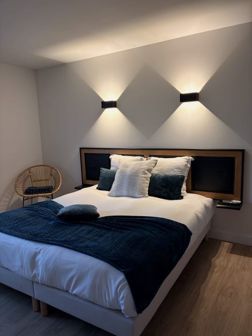 Chambre moderne de l'Hôtel les Vieilles Pierres à Eymet : lit, appliques murales, fauteuil en rotin et parquet