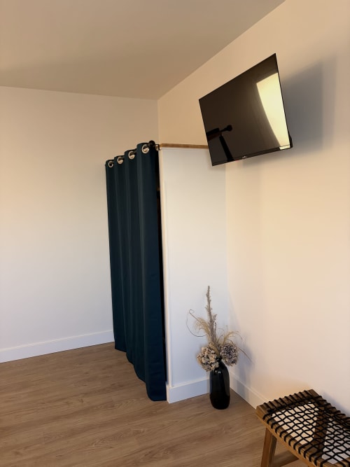 Chambre moderne à l'Hôtel les Vieilles Pierres avec TV murale, rideaux épais, fleurs séchées en vase et chaise tressée
