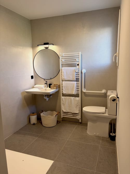 Salle de bains accessible moderne à l'Hôtel les Vieilles Pierres d'Eymet avec lavabo, toilettes, sèche-serviettes et douche