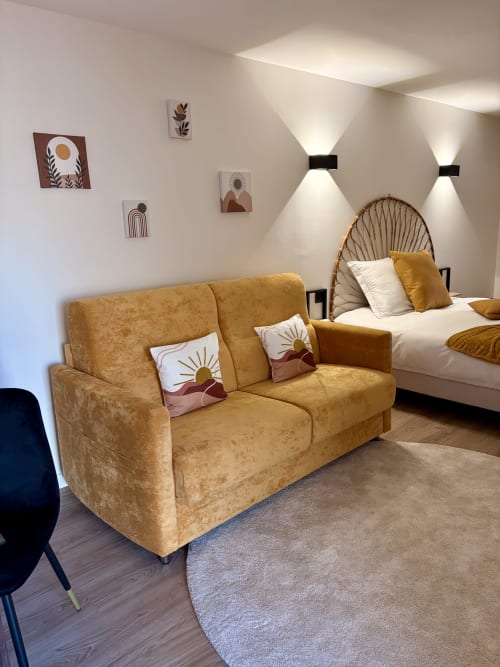 Chambre moderne à l'Hôtel les Vieilles Pierres à Eymet : canapé doré, lit-fauteuil tissé et décoration murale bohème