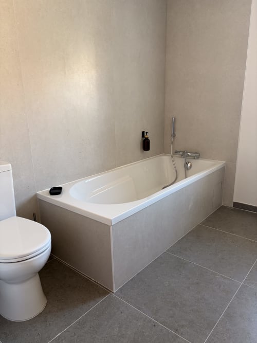 Salle de bain moderne avec baignoire blanche, toilettes et carrelage gris à l'Hôtel les Vieilles Pierres à Eymet, France