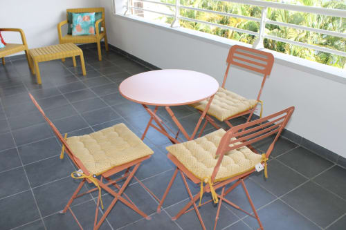 Coin salon sur balcon avec chaises métalliques orange, coussins crème et table ronde blanche donnant sur le jardin de Maisons En Or