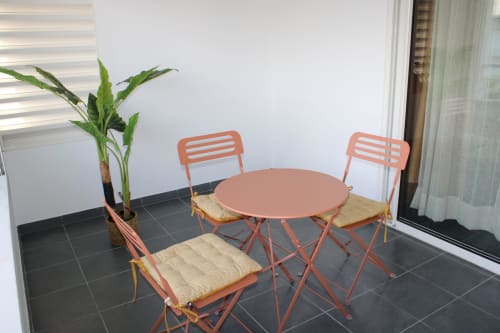 Balcon couvert avec chaises en métal corail, table ronde et plante en pot à Maisons En Or à Cayenne