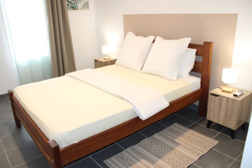 Chambre moderne avec lit en bois, draps blancs et tête de lit beige aux Maisons En Or à Cayenne, Guyane