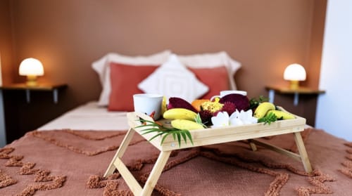 Chambre de luxe avec plateau de fruits de bienvenue, oreillers rouges et éclairage ambiant aux Maisons En Or, Cayenne