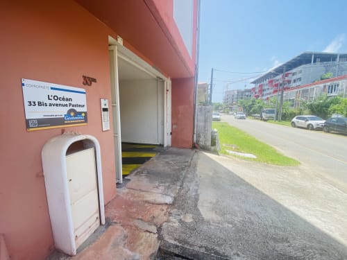 Entrée du bâtiment L'Océan au 33 bis avenue Pasteur, Cayenne, avec façade rouge et parking