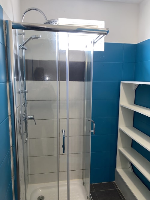 Salle de bain moderne aux carrelages bleus, douche vitrée, pommeau de douche pluie et rangements blancs à Cayenne