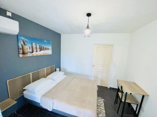 Chambre moderne à Maisons En Or Cayenne avec mur d'accent bleu-vert, literie blanche, tête de lit géométrique, suspension et espace repas