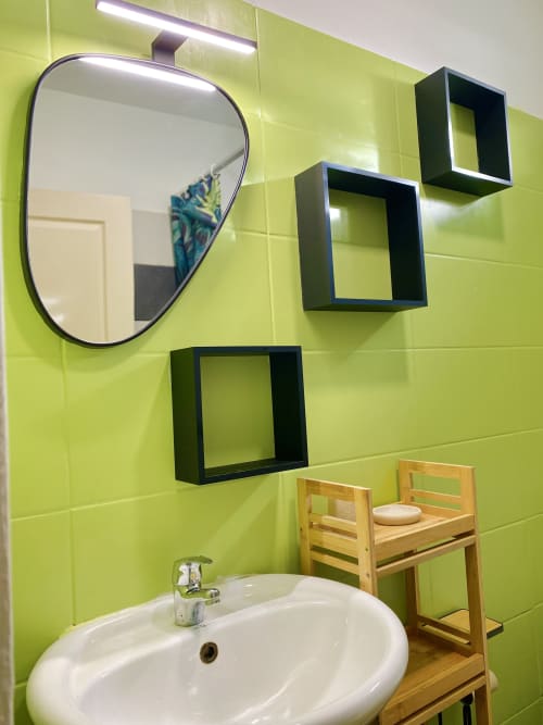 Salle de bain moderne dans un appartement de Cayenne avec murs carrelés vert citron, miroir rond, étagères flottantes noires et lavabo blanc