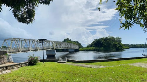Maisons En Or à Sinnamary, Guyane : Pont métallique traversant la rivière avec pelouse verdoyante et végétation tropicale