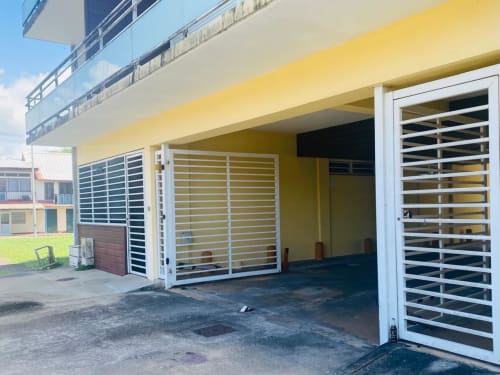 Cour de la résidence Maisons En Or à Sinnamary avec bâtiment jaune, portes blanches à jalousies et zone de stationnement
