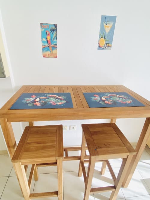 Table à manger en bois avec deux chaises et sets de table décorés à l'appartement Maisons En Or à Sinnamary, art tropical au mur