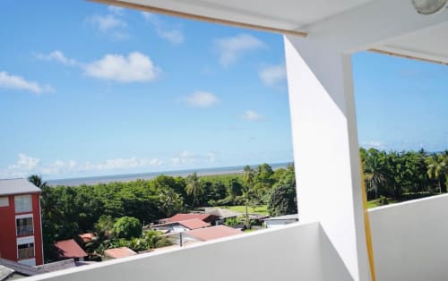 Vue du balcon de l'appartement Maisons En Or à Cayenne avec vue sur la mer, végétation tropicale et palmiers