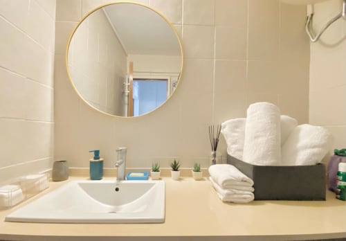 Salle de bain moderne dans un appartement à Cayenne avec miroir rond doré, lavabo blanc, rangements pour serviettes et vue sur la mer
