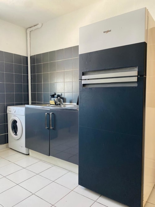 Kitchenette moderne avec réfrigérateur Whirlpool, meubles sombres, lave-linge et dosseret carrelé à l'appartement Cayenne