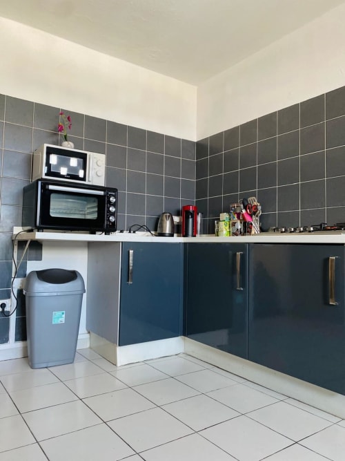 Coin cuisine moderne aux murs carrelés sombres, micro-ondes, four et électroménagers en acier inoxydable dans un appartement à Cayenne