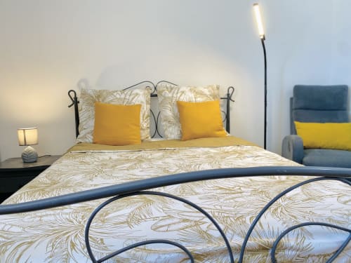 Chambre lumineuse avec oreillers jaunes, literie motifs, lit en métal, lampe de bureau et fauteuil aux Maisons En Or, Cayenne