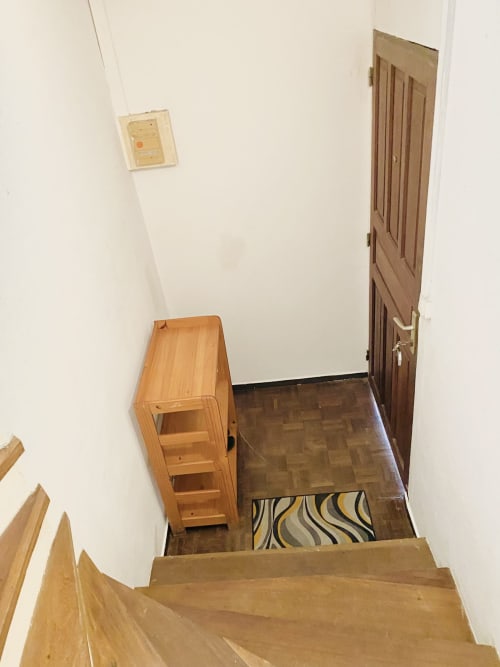 Entrée d'escalier dans un appartement de Cayenne avec armoire de rangement en bois, tapis rayé et porte en bois donnant sur un espace meublé