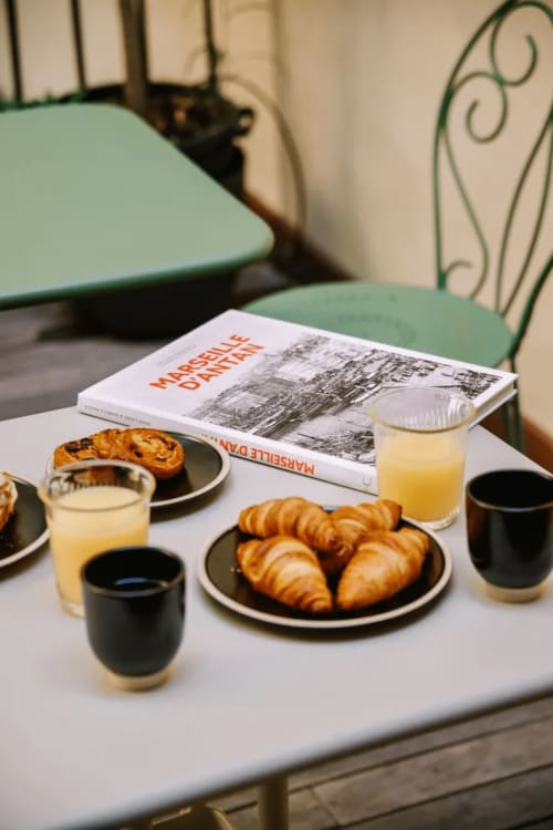 Tavolo colazione all'Hôtel Boutique Provencia a Marsiglia con cornetti, caffè, succo d'arancia e libro di architettura.