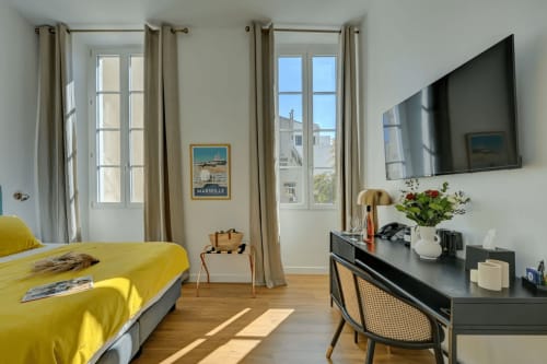 Luminosa camera d'hotel al Boutique Hôtel Provencia di Marsiglia con letto giallo, doppia finestra, scrivania nera e TV a parete