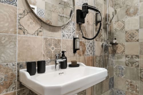 Bagno moderno del Boutique Hôtel Provencia a Marsiglia con piastrelle decorative, lavabo bianco e rubinetteria nera.