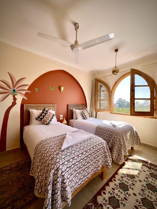 Deux lits jumeaux dans la chambre Lina Deluxe de la Dar Lina Guest House à Louxor, avec niche terracotta cintrée et vue sur le jardin
